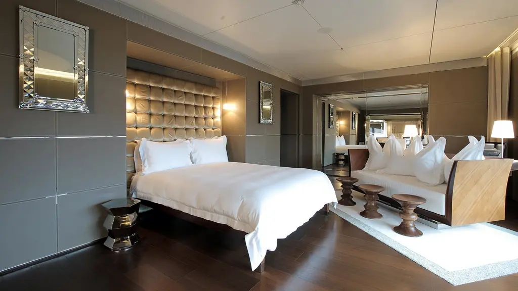 Stateroom with a padded headboard, grey walls, a mirror and a sofa with stools