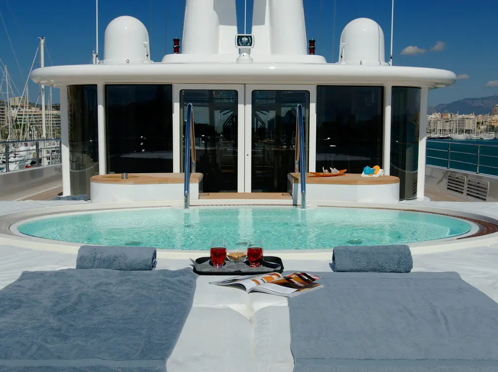A round pool on an open deck in front of glass doors, with grey loungers and a tray on the deck