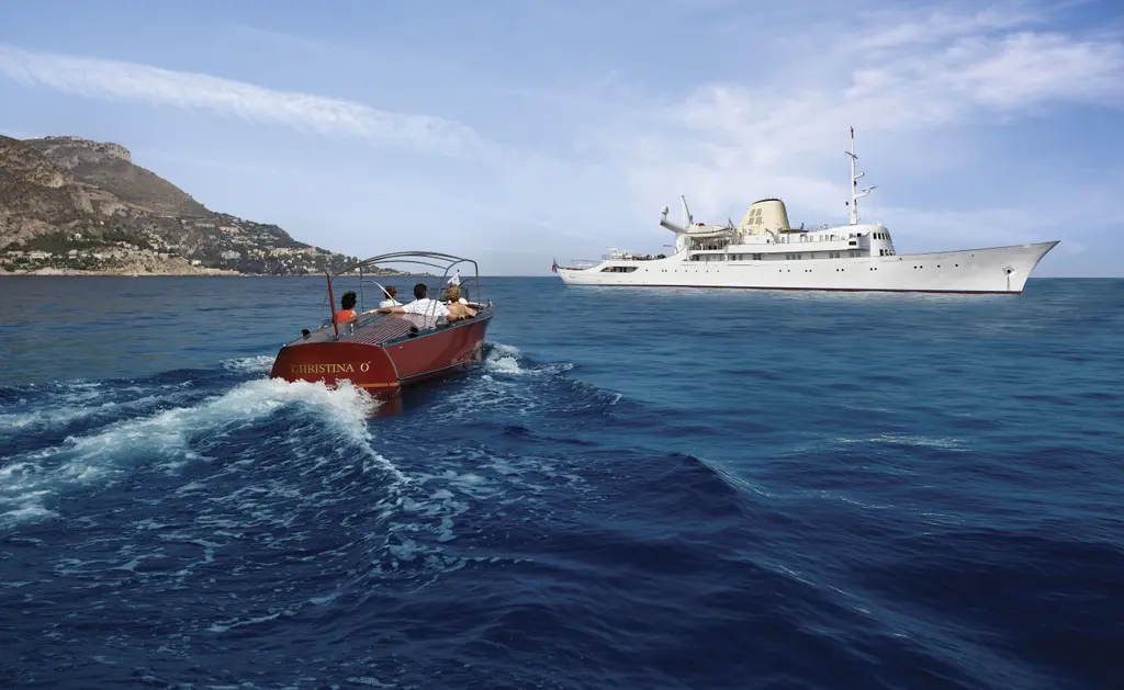 A classic wooden tender speeding away from Christina O, anchored off a rocky coastline
