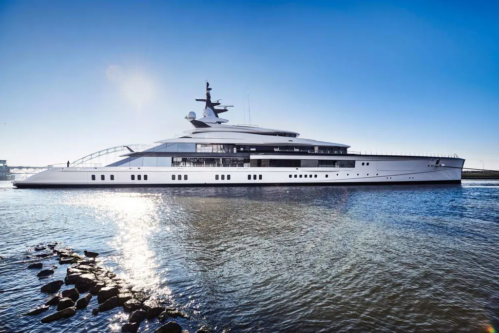 Bravo Eugenia in starboard profile on calm water in sunshine, with a bridge in the background