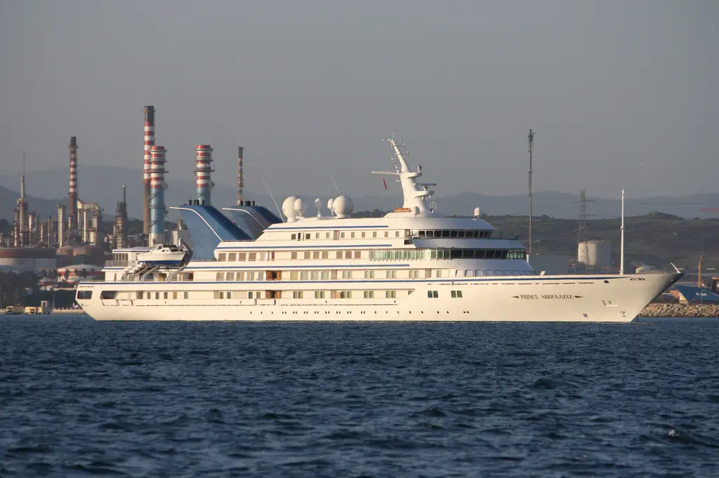 Prince Abdulaziz at anchor in starboard profile, with a tender on the aft deck and refinery chimneys behind