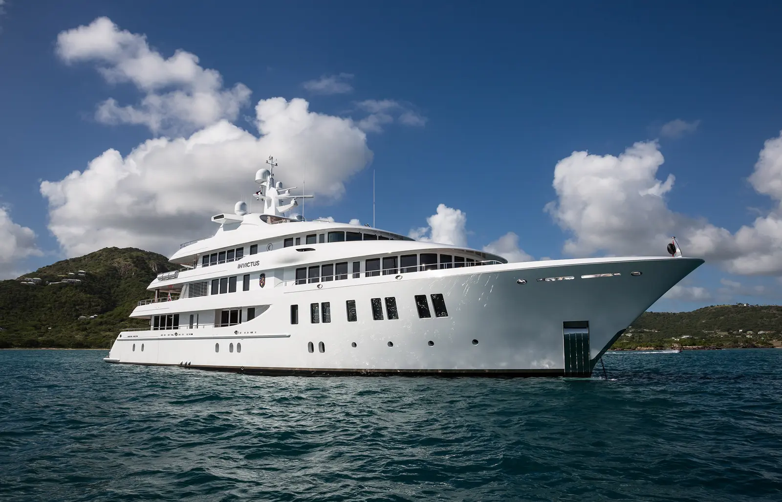 Invictus at anchor seen from the bow quarter, green hills behind