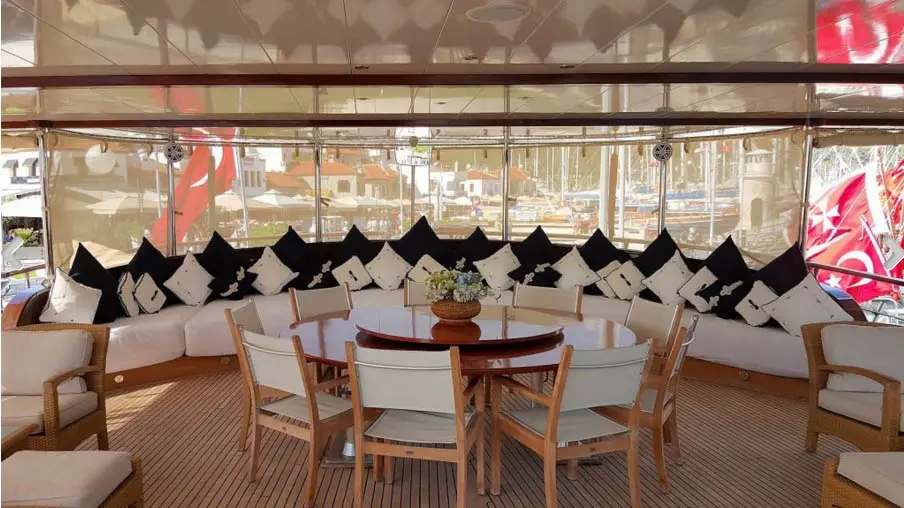 Round dining table on the aft deck with a long cushioned sofa along the stern