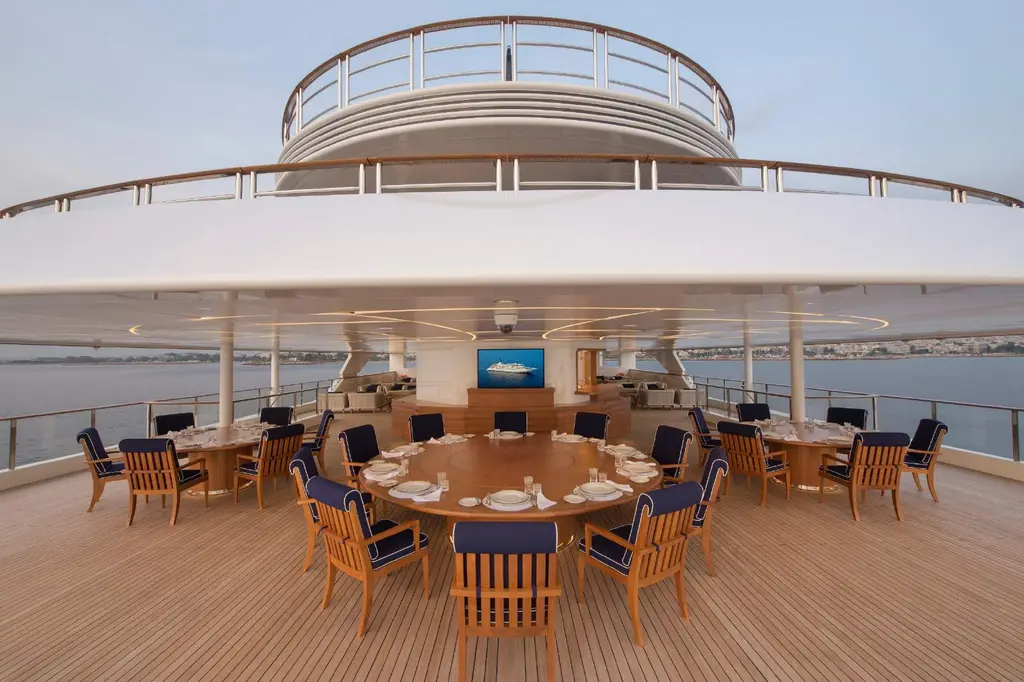 Round dining tables set on a teak aft deck under the deck overhang