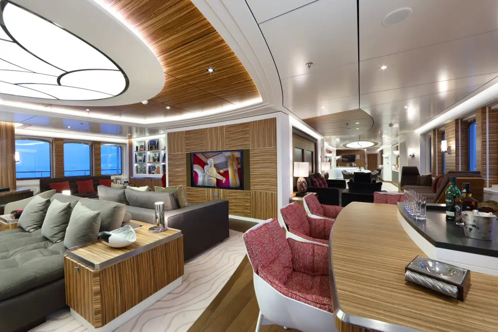 Saloon with grey sofas, red armchairs and a bar, under a curved wooden ceiling with a large backlit panel
