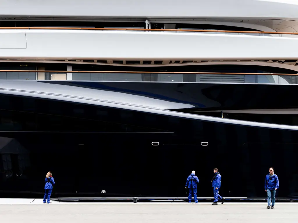 Yard workers in blue overalls walking along the quay beside the dark hull side of Breakthrough