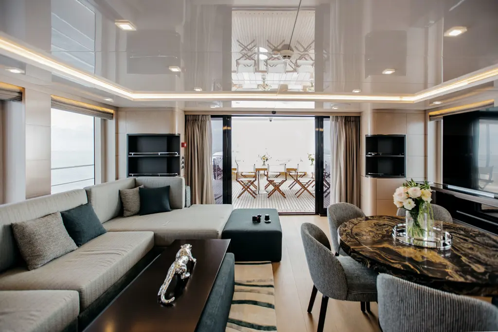 Sky lounge with a grey sofa, a round stone-topped table and glass doors opening to the aft deck