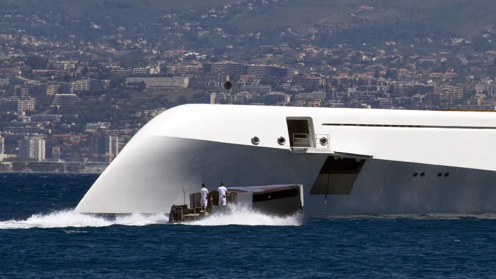 The bow of Motor Yacht A with a tender alongside and two crew aboard, a city behind