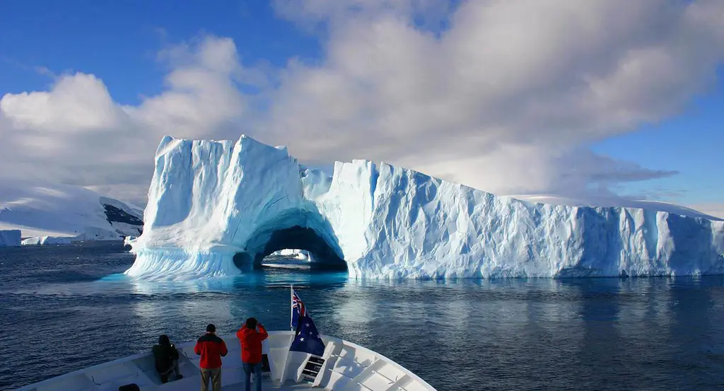 Guests in red jackets on Hanse Explorer's foredeck looking at an iceberg with an arch carved through it